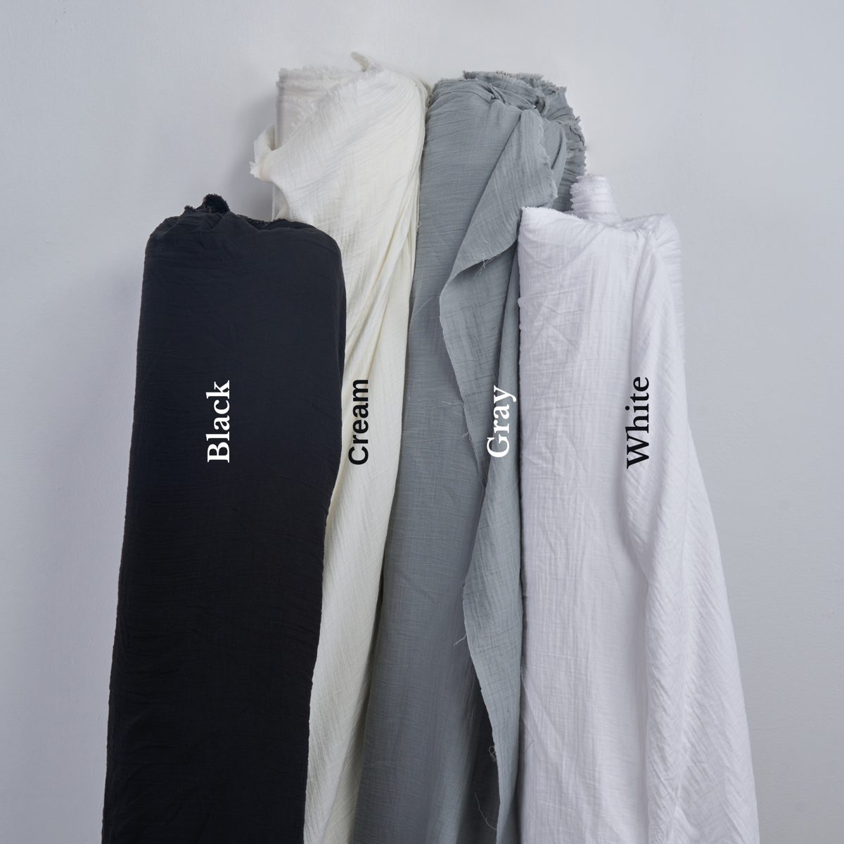 A row of cotton gauze fabric rolls in black, cream, grey, and white.
