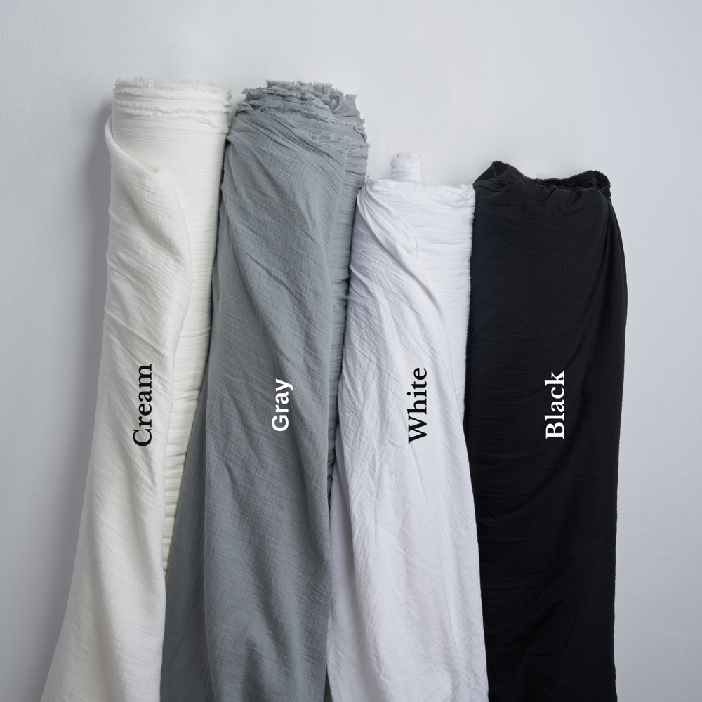 Cotton gauze fabric rolls in black, cream, grey, and white arranged side by side.