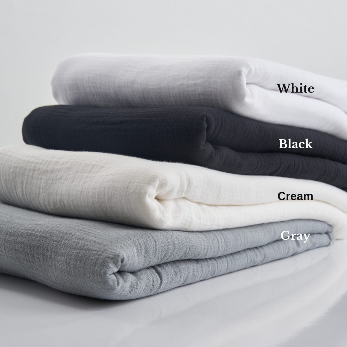 Four colors of folded crinkled cotton gauze fabrics stacked neatly on top of each other.
