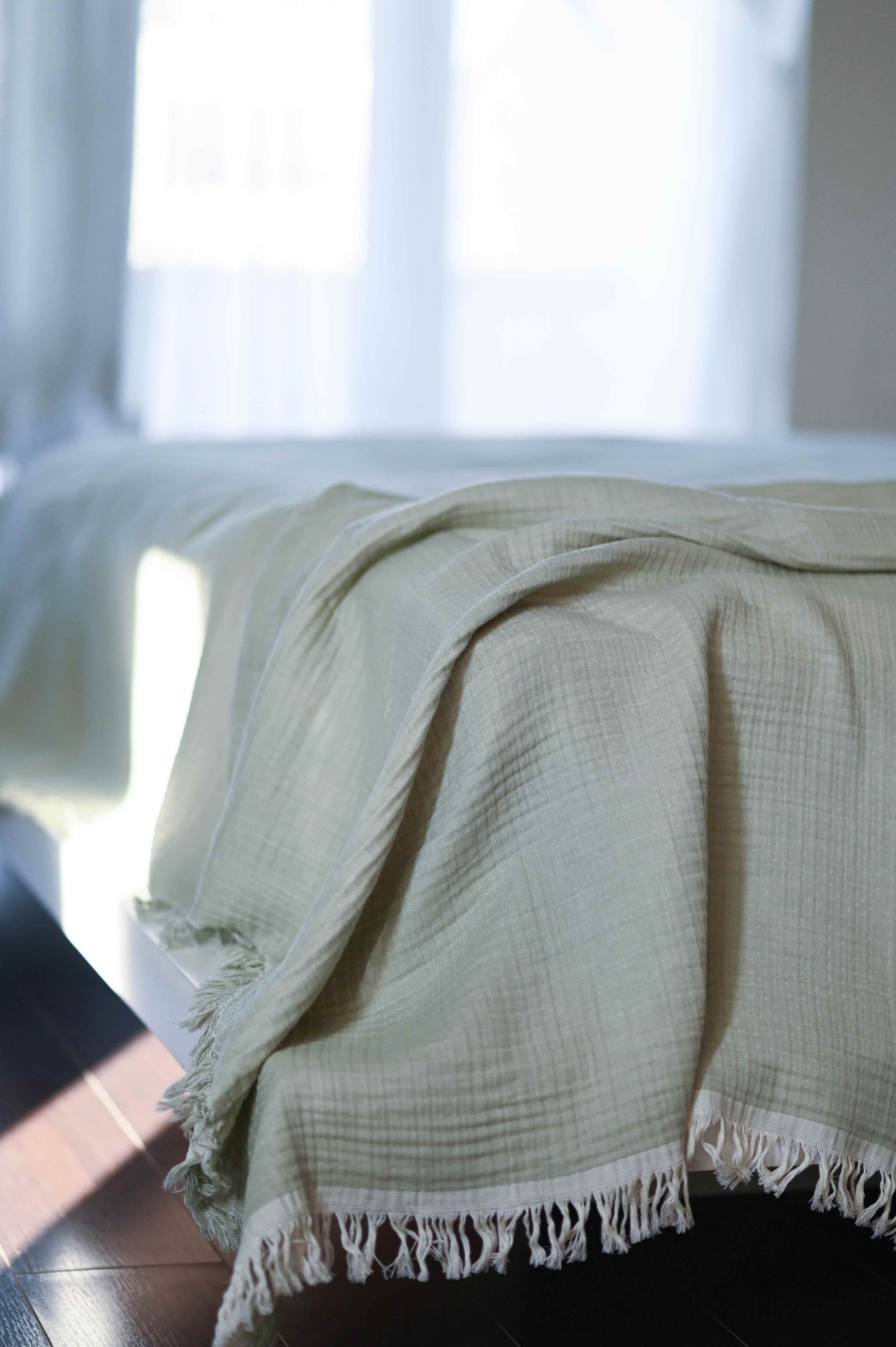 Double-sided muslin blanket in soothing sage green and ecru tones with fringe details