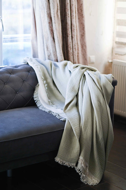 Double-sided muslin blanket in soothing sage green and ecru tones with fringe details