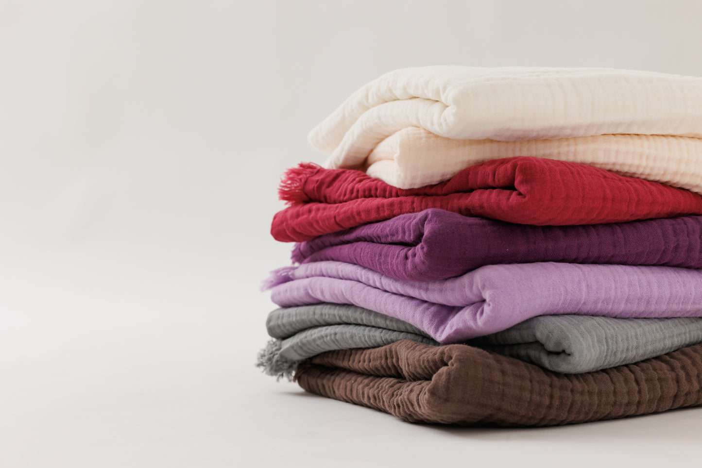 Six colorful crinkled cotton blankets stacked neatly together