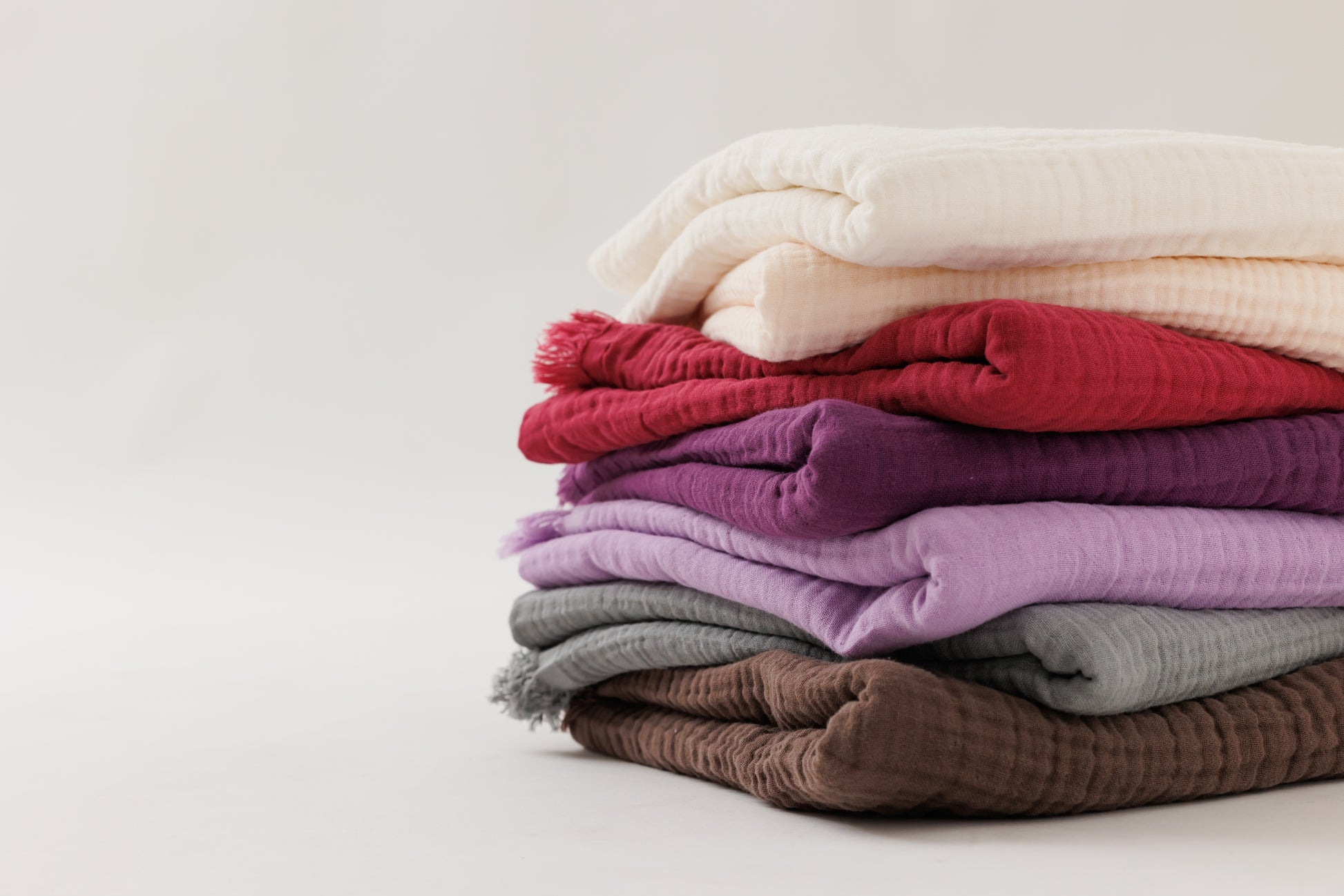 Six colorful crinkled cotton blankets stacked neatly together