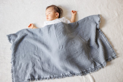 Gray crinkled muslin blanket styled on a bed, showing its versatility as a bedspread or throw.