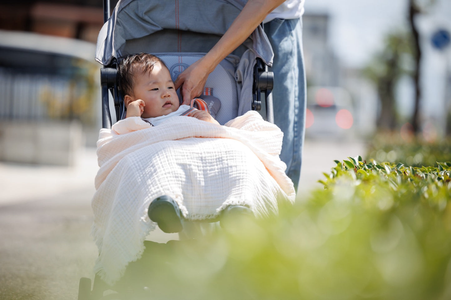 Cream-colored organic muslin blanket used as a lightweight travel cover, demonstrating its portability and comfort