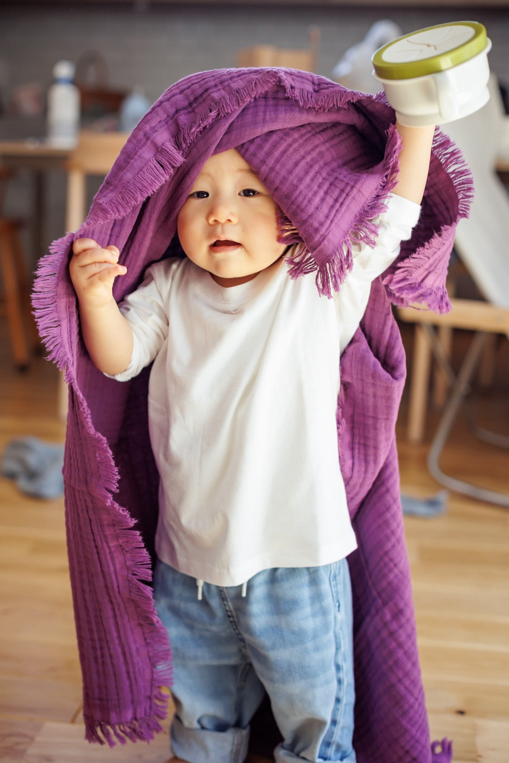 Baby wrapped in an organic cotton purple blanket, playing and smiling